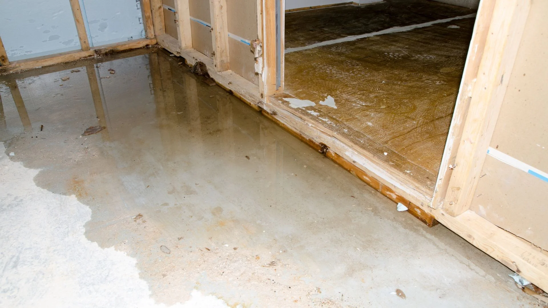 A flooded basement shows water pooling on the floor, near unfinished walls and exposed wooden framing.
